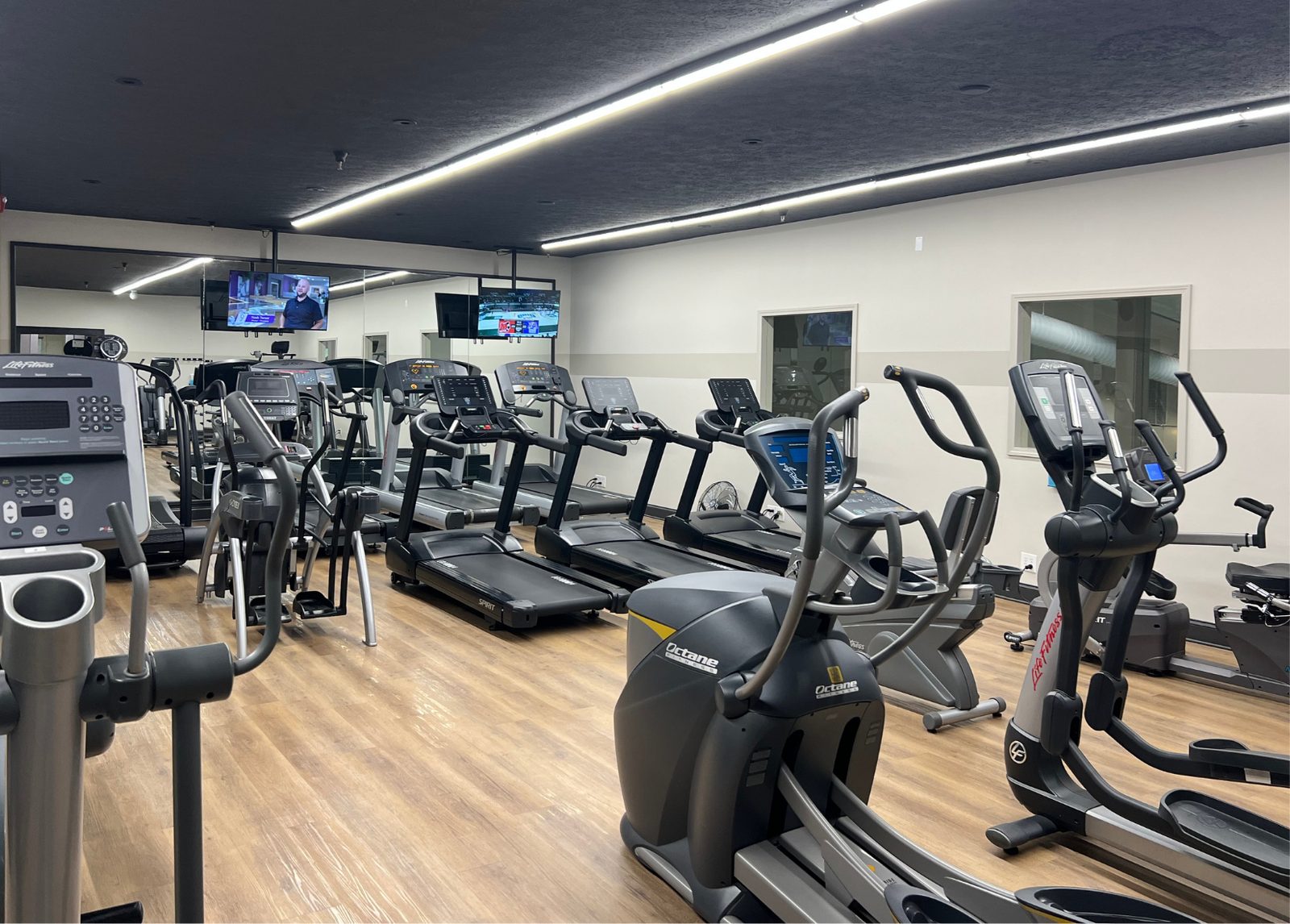The cardio room at The Club — treadmills, ellipticals and bikes on a wood floor