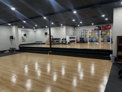 The class studio at The Club — open wood floor with stability balls along the wall